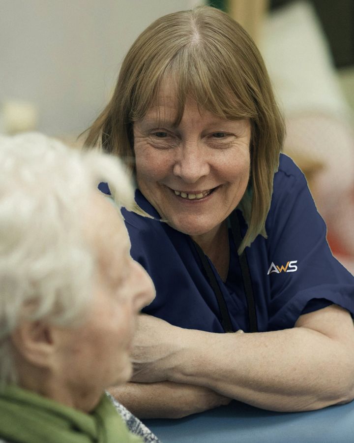 A carer in a navy AWS uniform sharing a smile with an older woman