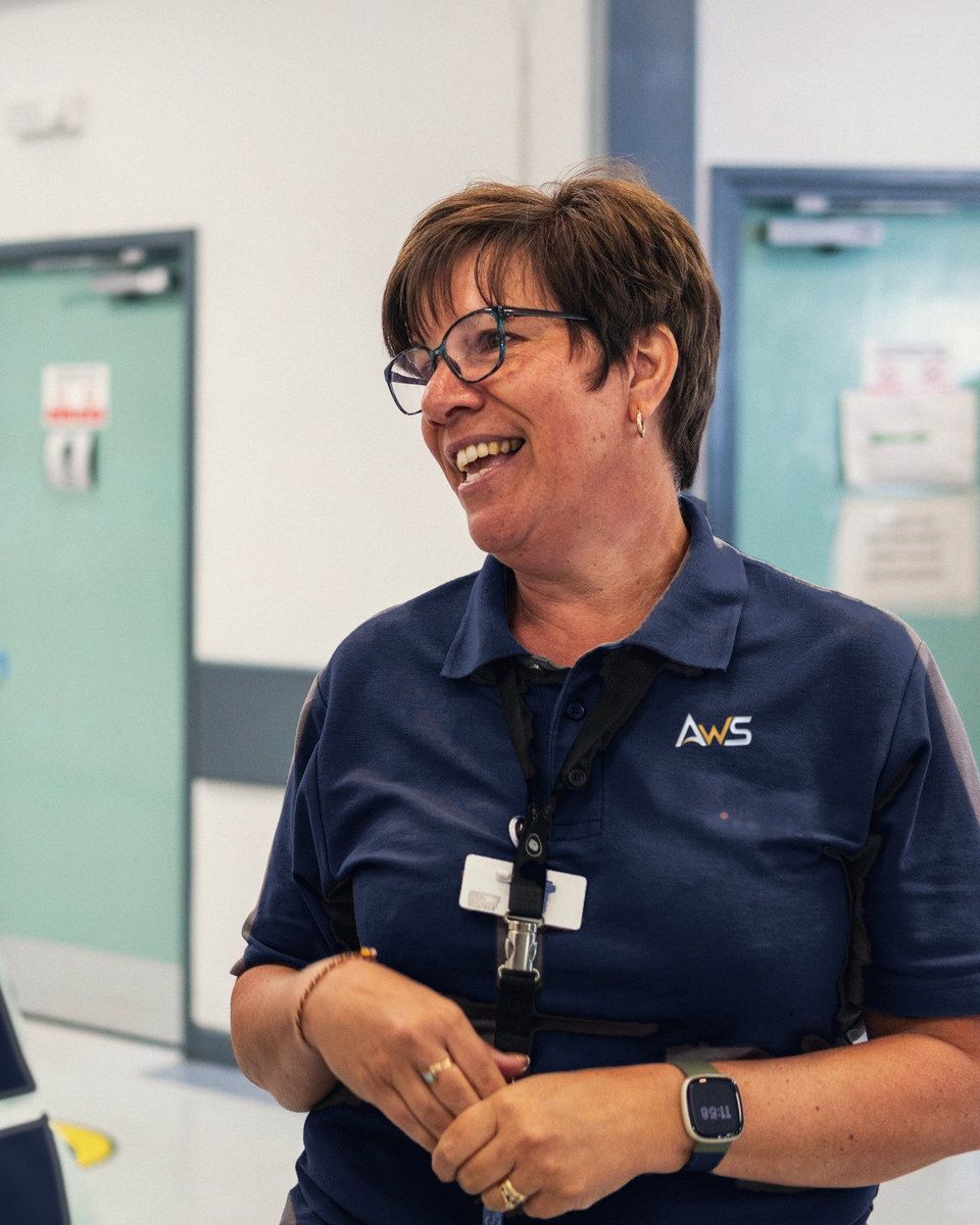 A care worker in a navy AWS uniform, smiling as she talks with a colleague
